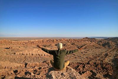 Rear view of man walking in desert against clear sky