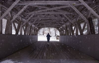 Rear view of woman standing on covered bridge during snowfall