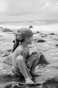 Woman sitting on rock at beach against sky