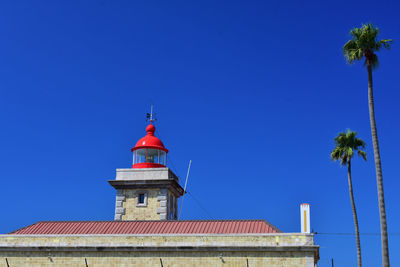 Low angle view of lighthouse by building against clear blue sky