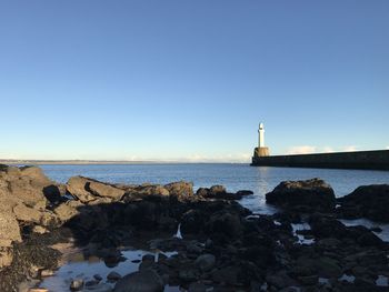 Lighthouse by sea against clear blue sky