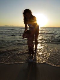 Young woman standing on beach against sky during sunset