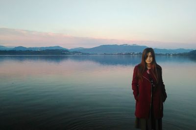 Young woman standing against lake during sunset