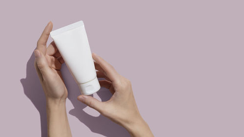 Young female hands holding blank white squeeze bottle plastic tube on pink background. mockup. 