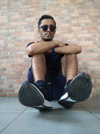 Portrait of man wearing sunglasses sitting against brick wall