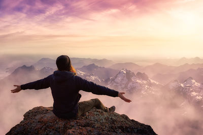 Rear view of man on rock against sky during sunset