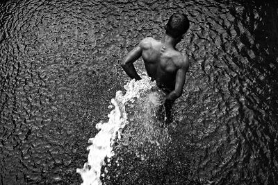 Rear view of shirtless man standing in water