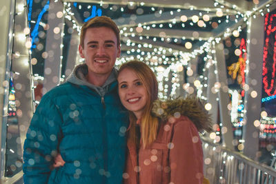 Portrait of smiling young couple standing outdoors during christmas at night