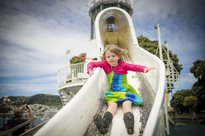 Low angle view of girl sliding on slide at playground against sky