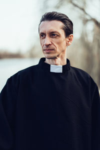 Priest looking away while standing against sky
