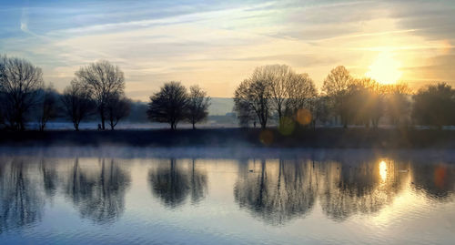 Reflection of silhouette trees on water against sky