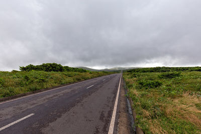 Road amidst field against sky during rainy season