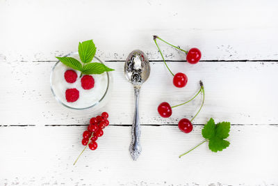 A glass with milk yogurt, ripe raspberries, a green leaf, red currant berries and cherries on white