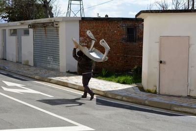 Rear view of man carrying metal on road
