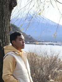 Young man looking away while standing on tree against the fuji mountain 