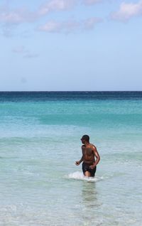 Shirtless man walking in sea against sky