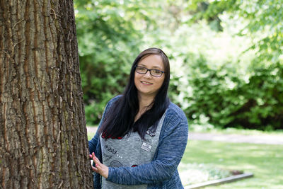 Portrait of smiling woman standing by tree at park
