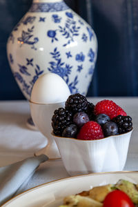 Mixed berries and a soft boiled egg for breakfast on a table with a blue vase.