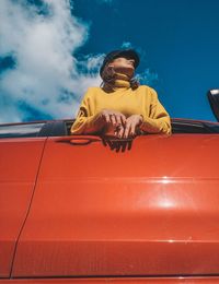 Low angle view of woman leaning from car window against sky