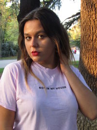 Portrait of teenage girl standing against tree trunk