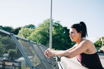 Side view of exhausted sportswoman leaning on railing at bridge