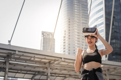 Young woman using virtual reality simulator standing against building in city