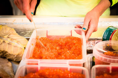 Midsection of woman picking caviar from container at market