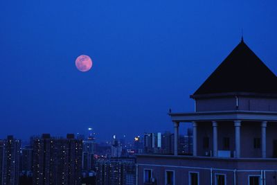 Illuminated buildings against blue sky at night