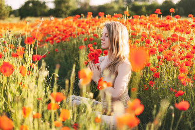 A beautiful girl with closed eyes meditates on a poppy field holding a bouquet of flowers