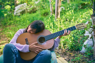 Smiling woman holding guitar against plants