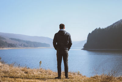 Rear view of man looking at lake against sky