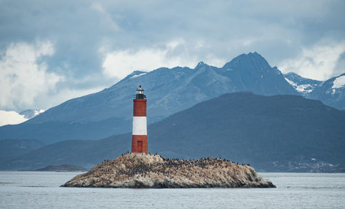 Lighthouse by sea against mountain range against sky