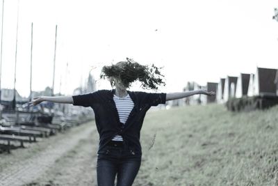 Woman throwing grass while standing on field against clear sky