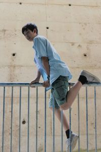 Side view of boy on railing against wall