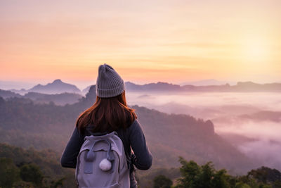 Rear view of woman looking at mountains against sky during sunset