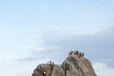 People on rock against cloudy sky