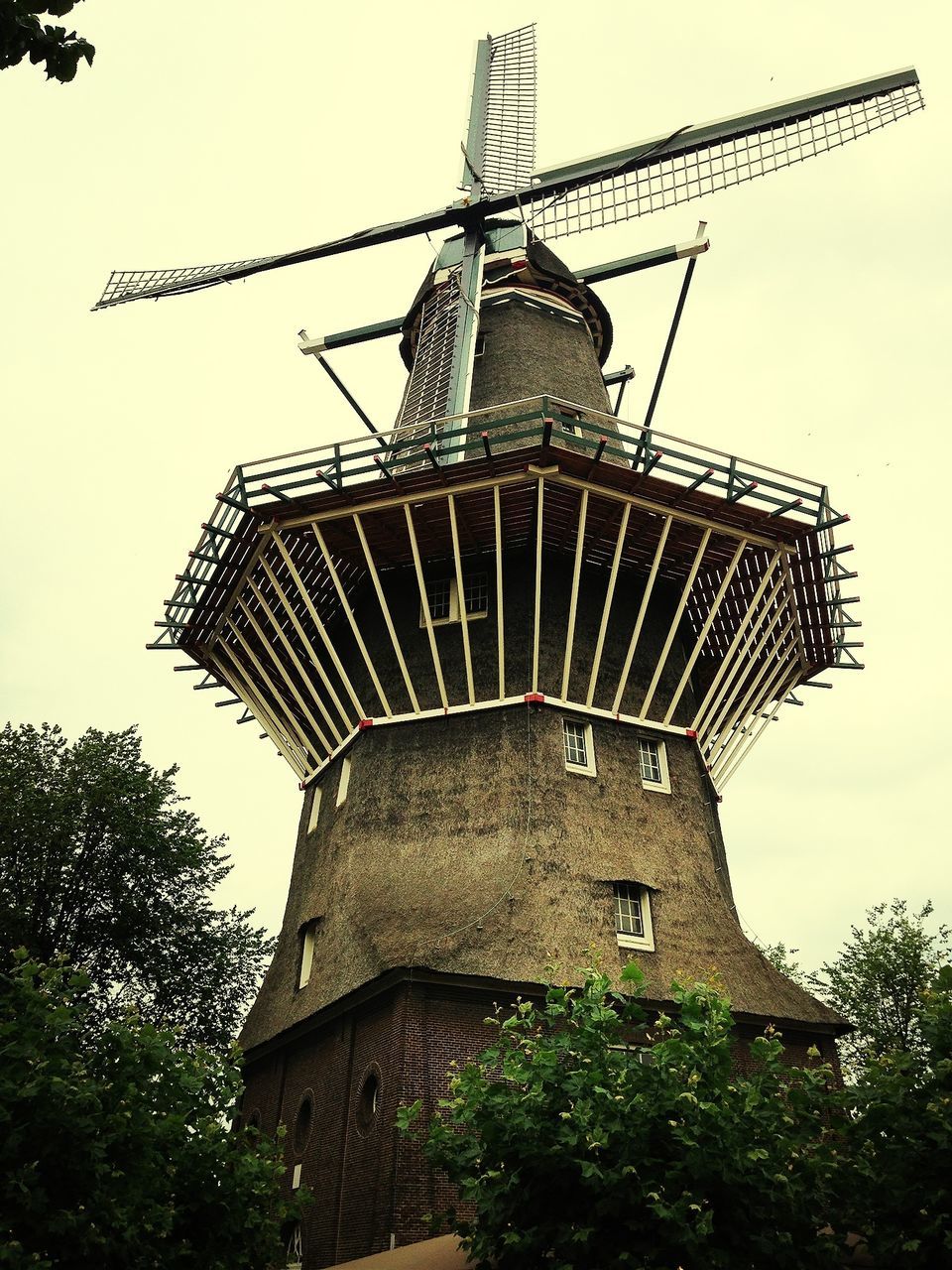 low angle view, built structure, architecture, building exterior, tree, religion, clear sky, spirituality, place of worship, sky, traditional windmill, cross, day, outdoors, tower, no people, windmill, church, history