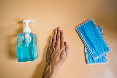 Close-up of hand holding bottle against blue wall