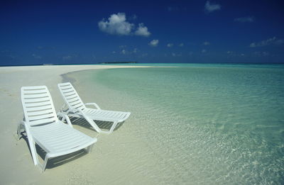 Empty lounge chairs at beach against sky