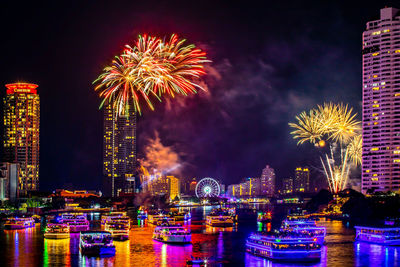 Firework display over illuminated city against sky at night