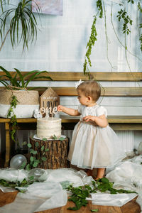 Full length of cute girl standing by cake at home