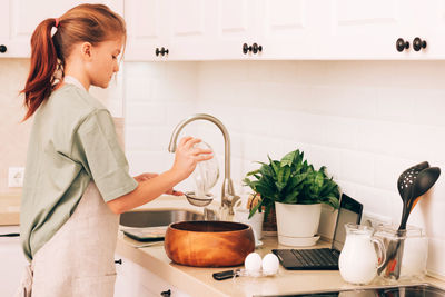 Side view of young woman using mobile phone in kitchen