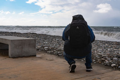 Rear view of man standing at beach against sky