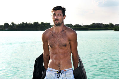 Wet shirtless man removing life jacket against lake