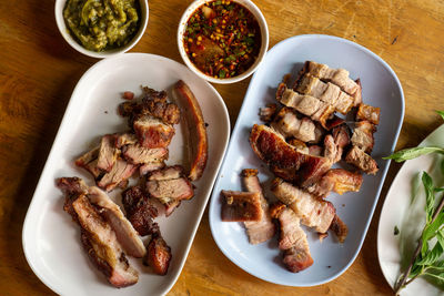 High angle view of roast pork meat and crispy pork belly on plate on wooden table with sauces