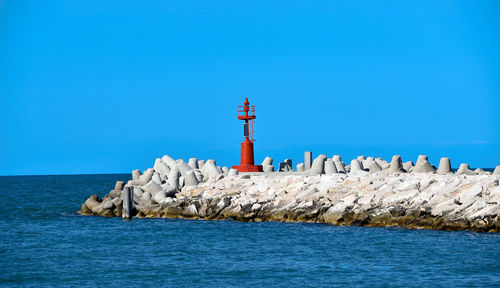 Lighthouse by sea against blue sky