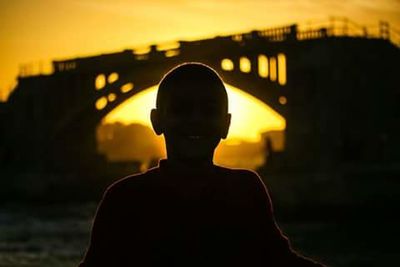 Silhouette of man on bridge against sunset sky