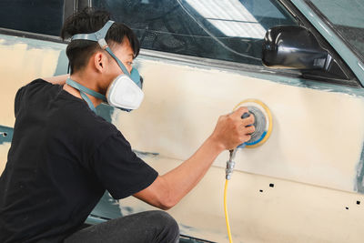 Young man working with equipment on car in garage