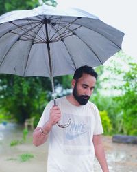 Young man with umbrella standing on rainy day