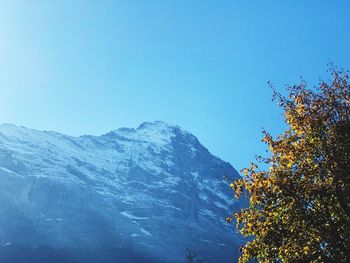 Low angle view of snowcapped mountains against clear blue sky